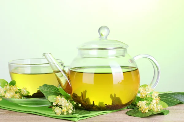 Teapot and cup with linden tea and flowers on wooden table on green background — Stock Photo, Image
