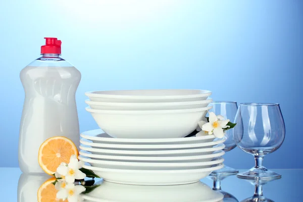 Pratos limpos vazios e copos com líquido de lavar louça e limão no fundo azul — Fotografia de Stock