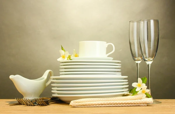 Assiettes propres vides, verres et tasse sur table en bois sur fond gris — Photo