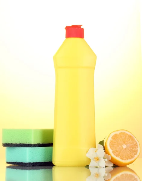 Líquido lavavajillas con esponjas y limón con flores sobre fondo amarillo —  Fotos de Stock