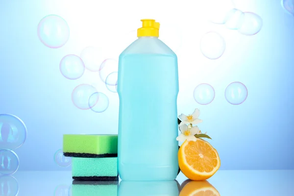 Líquido de lavagem de pratos com esponjas e limão com flores em fundo azul — Fotografia de Stock
