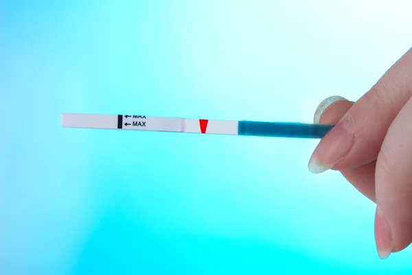 Test de grossesse en main sur fond bleu — Photo