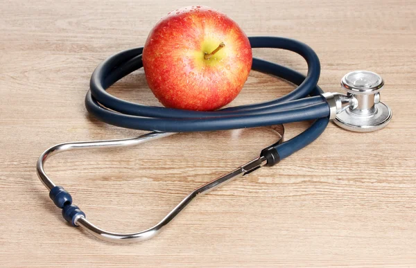 Medical stethoscope and red apple on wooden background — Stock Photo, Image