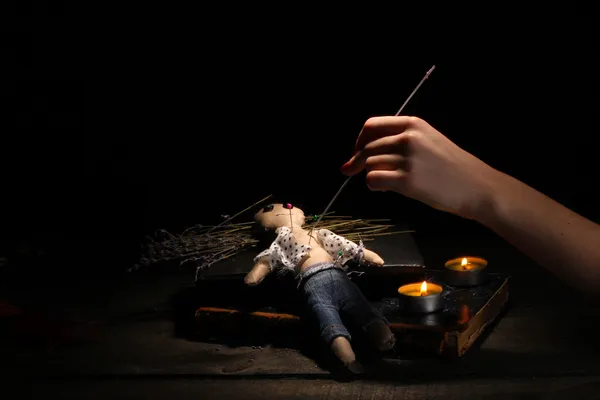 Voodoo panenka kluk propíchnout jehlou na dřevěný stůl ve světle svíček — Stock fotografie