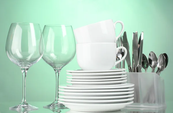 Чистые тарелки, стаканы, чашки и столовые приборы на зеленом фоне — стоковое фото
