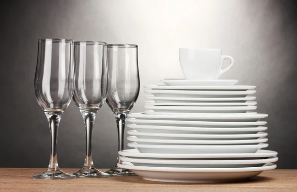 Platos limpios, vasos y taza sobre mesa de madera sobre fondo gris — Foto de Stock