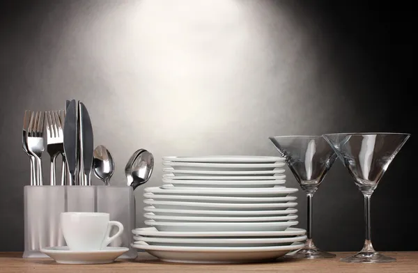 Čisté talíře, sklenice, pohár a příbory na dřevěný stůl na šedém pozadí — Stock fotografie