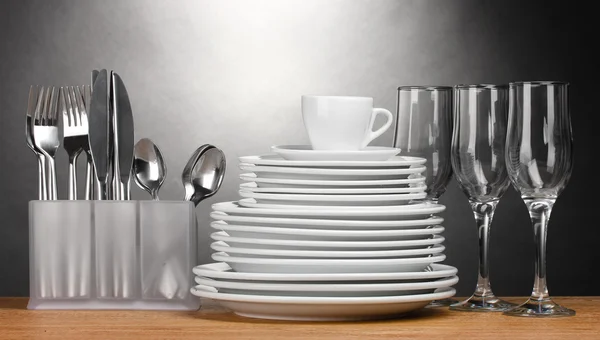 Clean plates, glasses, cup and cutlery on wooden table on grey background — Stock Photo, Image