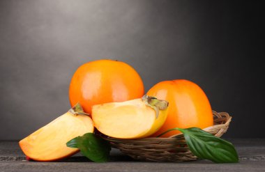 Appetizing persimmons in pad on wooden table on grey background clipart