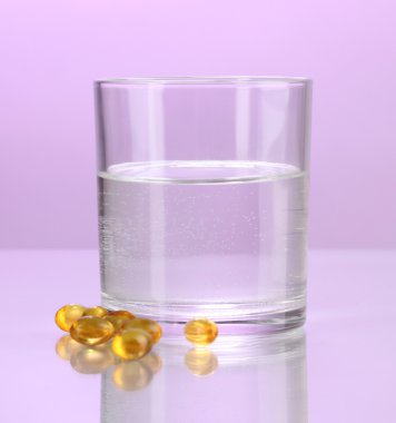 Glass of water and pills on purple background clipart