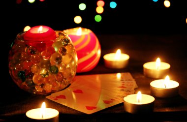 Candles and playing cards on wooden table on bright background clipart