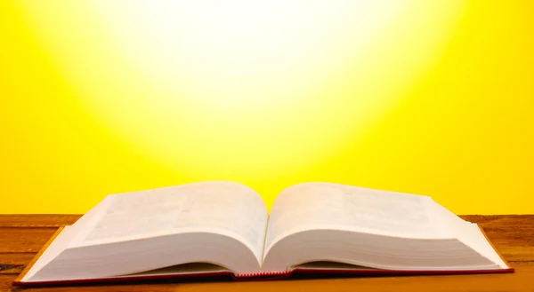 Açık kitap üzerine Sarı zemin üzerine ahşap masa — Stok fotoğraf