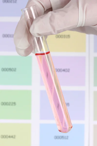 Tube with pink liquid in hand on color samples background — Stock Photo, Image