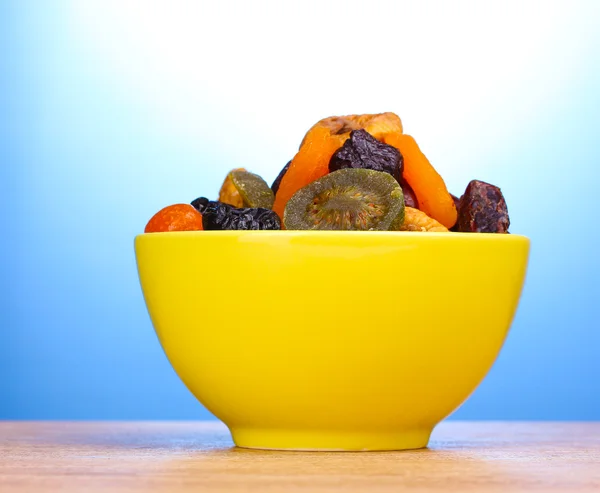 Gedroogde vruchten in heldere kom op houten tafel op blauwe achtergrond — Stockfoto