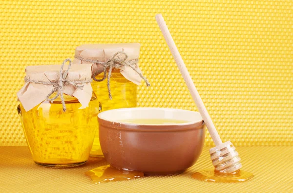 Jars of honey, bowl and wooden drizzler with honey on yellow honeycomb background — Stock Photo, Image