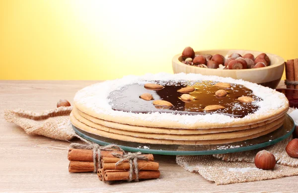 Kuchen auf Glasständer und Nüsse auf Holztisch auf gelbem Hintergrund — Stockfoto