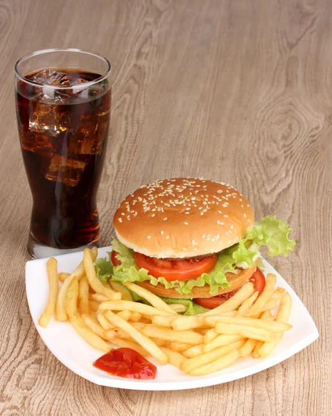 Hamburger grande e gustoso e patate fritte sul piatto con cola sul tavolo di legno — Foto Stock