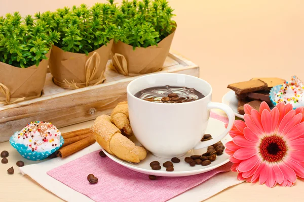 Cup of coffee and gerbera beans, cinnamon sticks on wooden table — Stock Photo, Image