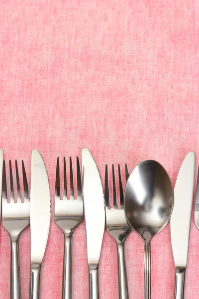 Vidličky, lžíce a nože na růžové ubrus — Stock fotografie