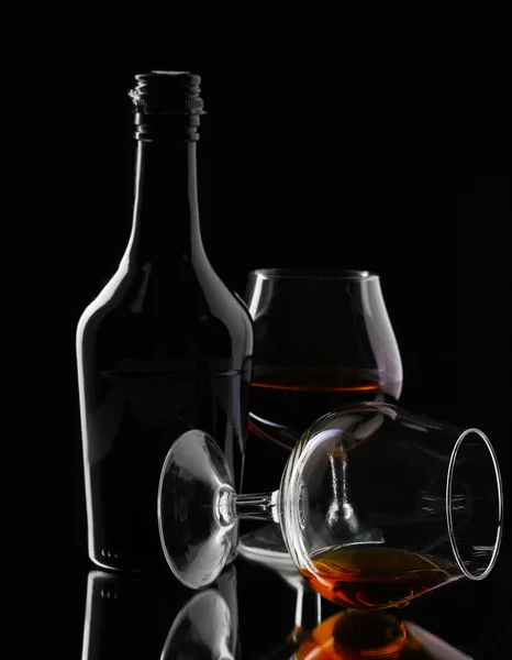 Vasos de brandy y botella sobre fondo negro — Foto de Stock