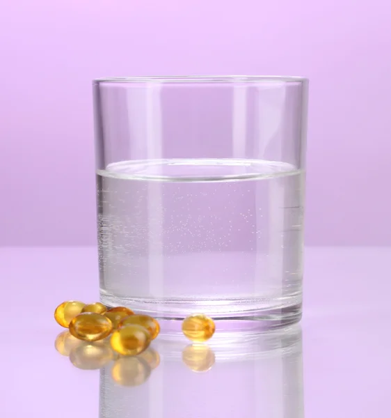 Стакан воды и таблетки на фиолетовом фоне — стоковое фото
