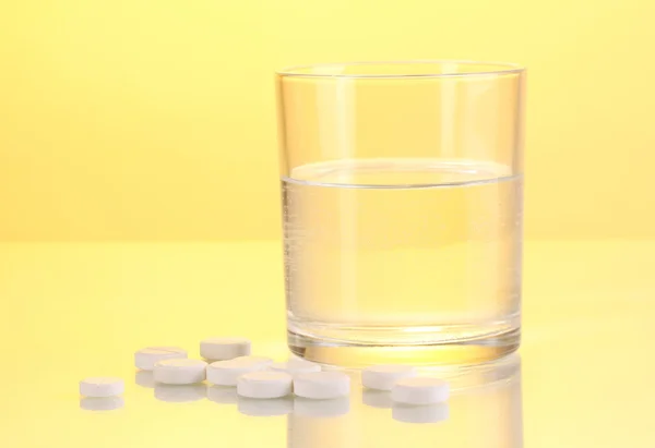 Glas vatten och piller på gul bakgrund — Stockfoto