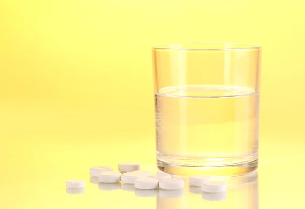 Szklanką wody i tabletki na żółtym tle — Zdjęcie stockowe