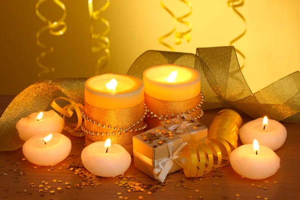 Belas velas, presentes e decoração em mesa de madeira no fundo amarelo — Fotografia de Stock