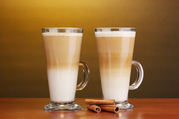 Geurige? offee latte in glazen bekers en kaneel op houten tafel op bruine achtergrond — Stockfoto