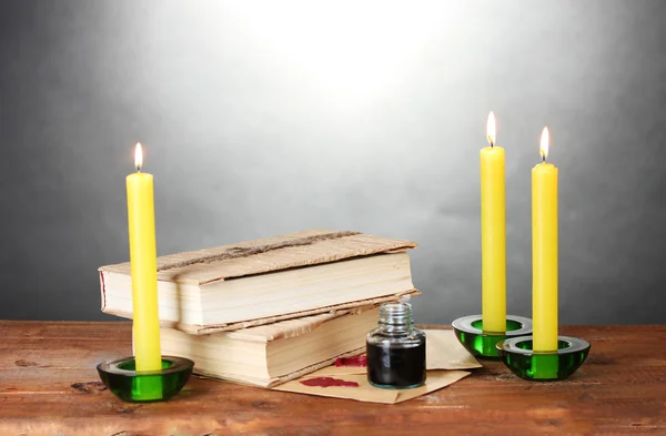 Alte Bücher, Schriftrollen, Tintenfass und Kerzen auf Holztisch auf grauem Hintergrund — Stockfoto