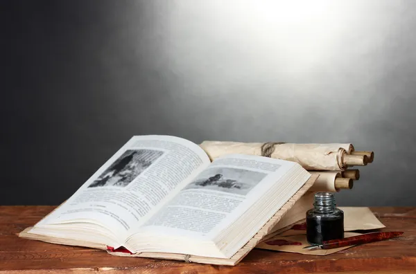 Oude boeken, rollen, inkt pen en inktpotje op houten tafel op grijze achtergrond — Stockfoto