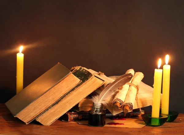 Staré knihy, svitky, peří pera inkwell a svíčky na dřevěný stůl na hnědé pozadí — Stock fotografie