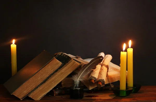 Old books, scrolls, feather pen inkwell and candles on wooden table on brown background — Stock Photo, Image