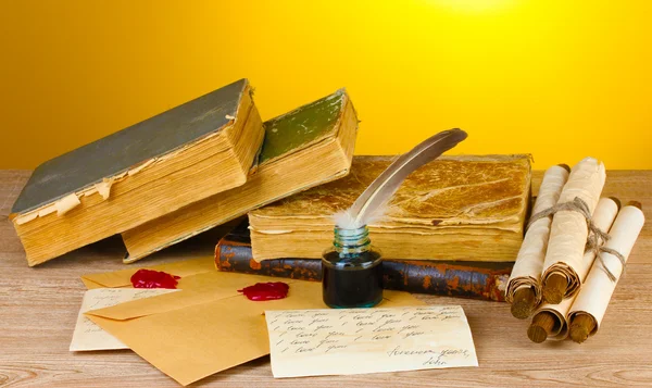 Old books, scrolls, feather pen and inkwell on wooden table on yellow background — Stok fotoğraf