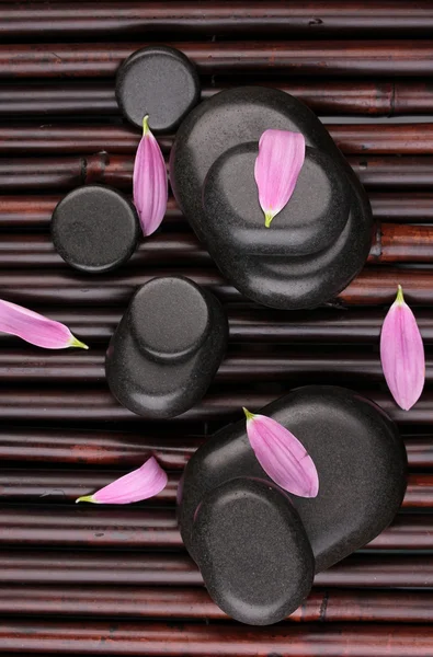 Piedras de spa y pétalos de flores en estera de bambú — Foto de Stock
