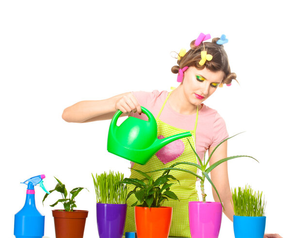 Beautiful happy young housewife watering plants in flowerpots isolated on white