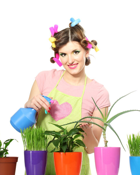 Beautiful happy young housewife sprays plants in flowerpots isolated on white