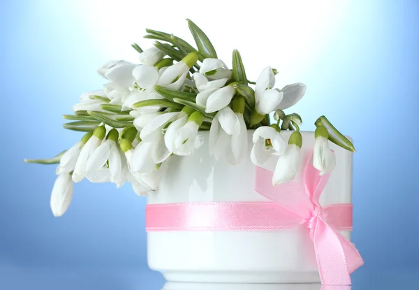 Krásnou kytici sněženky v váza s lukem na modrém pozadí — Stock fotografie