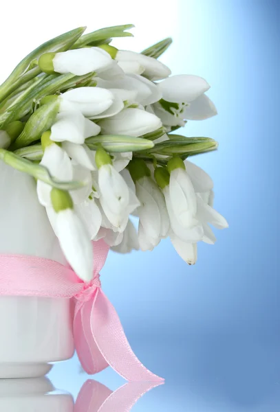 Schöner Strauß Schneeglöckchen in der Vase mit Schleife auf blauem Hintergrund — Stockfoto