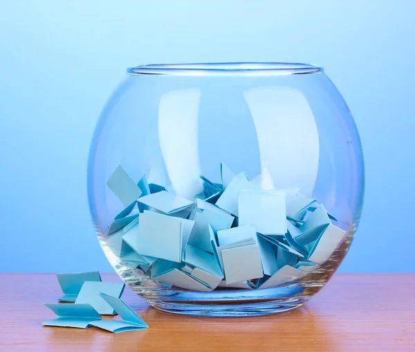 Кусочки бумаги для лотереи в вазе на деревянном столе на синем фоне — стоковое фото