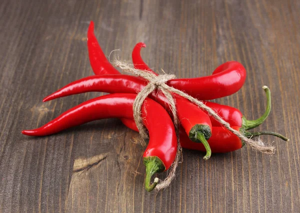 Red hot chili peppers bunden med rep på trä bakgrund — Stockfoto