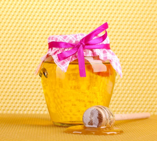 Jar of honey and wooden drizzler on yellow honeycomb background Stock Picture