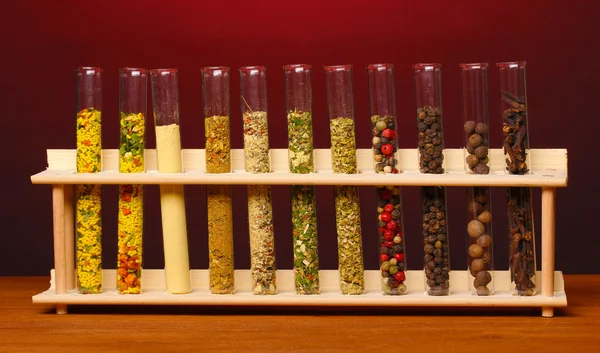 Olika kryddor i rören på träbord på röd bakgrund — Stockfoto