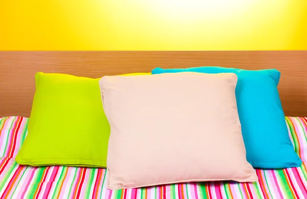 Bright pillows on bed on yellow background — Stock Photo, Image
