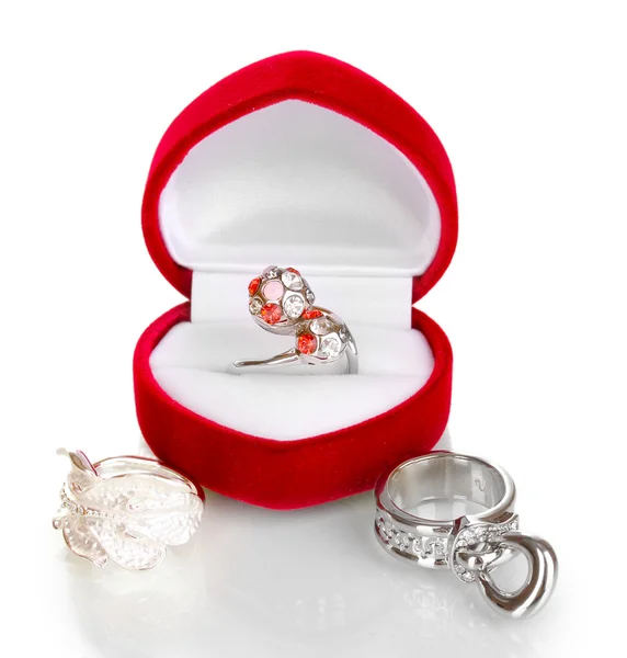 Anillo de plata con cristales rojos, rosados y claros en caja de terciopelo rojo y algunos anillos de plata aislados en blanco — Foto de Stock