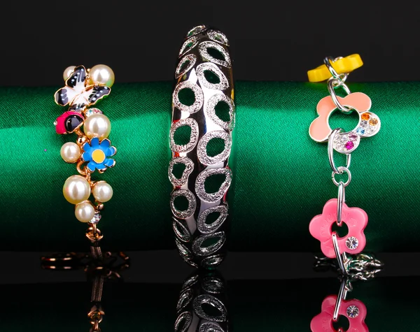 Três pulseiras de moda no pano verde no fundo preto — Fotografia de Stock