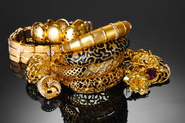 Schöne goldene Armbänder, Ringe und Schmuck auf grauem Hintergrund — Stockfoto