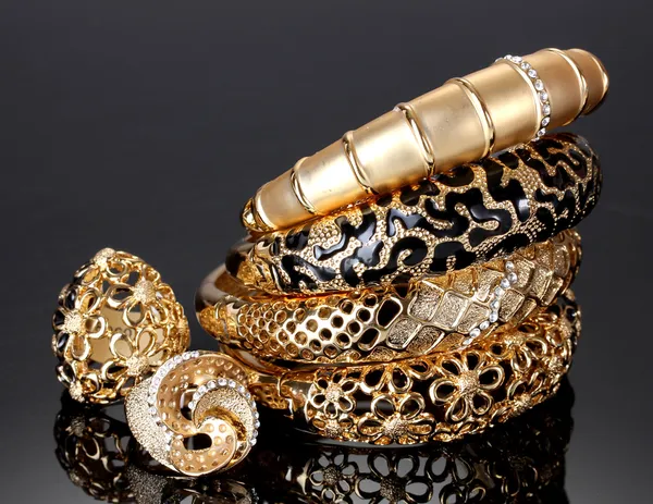 Belas pulseiras douradas e anéis no fundo cinza — Fotografia de Stock