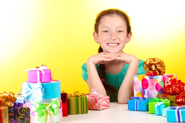 Little girl with gifts on yellow background — Stock Photo, Image