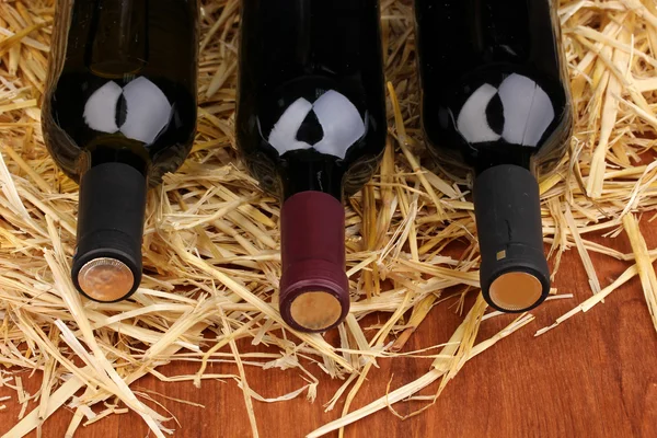 Bottles of great wine on hay on wooden table — Stock Photo, Image